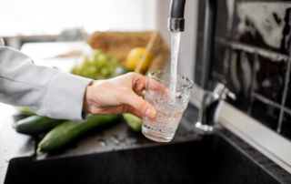 A person filling a clear cup with water from the kitchen's faucet.