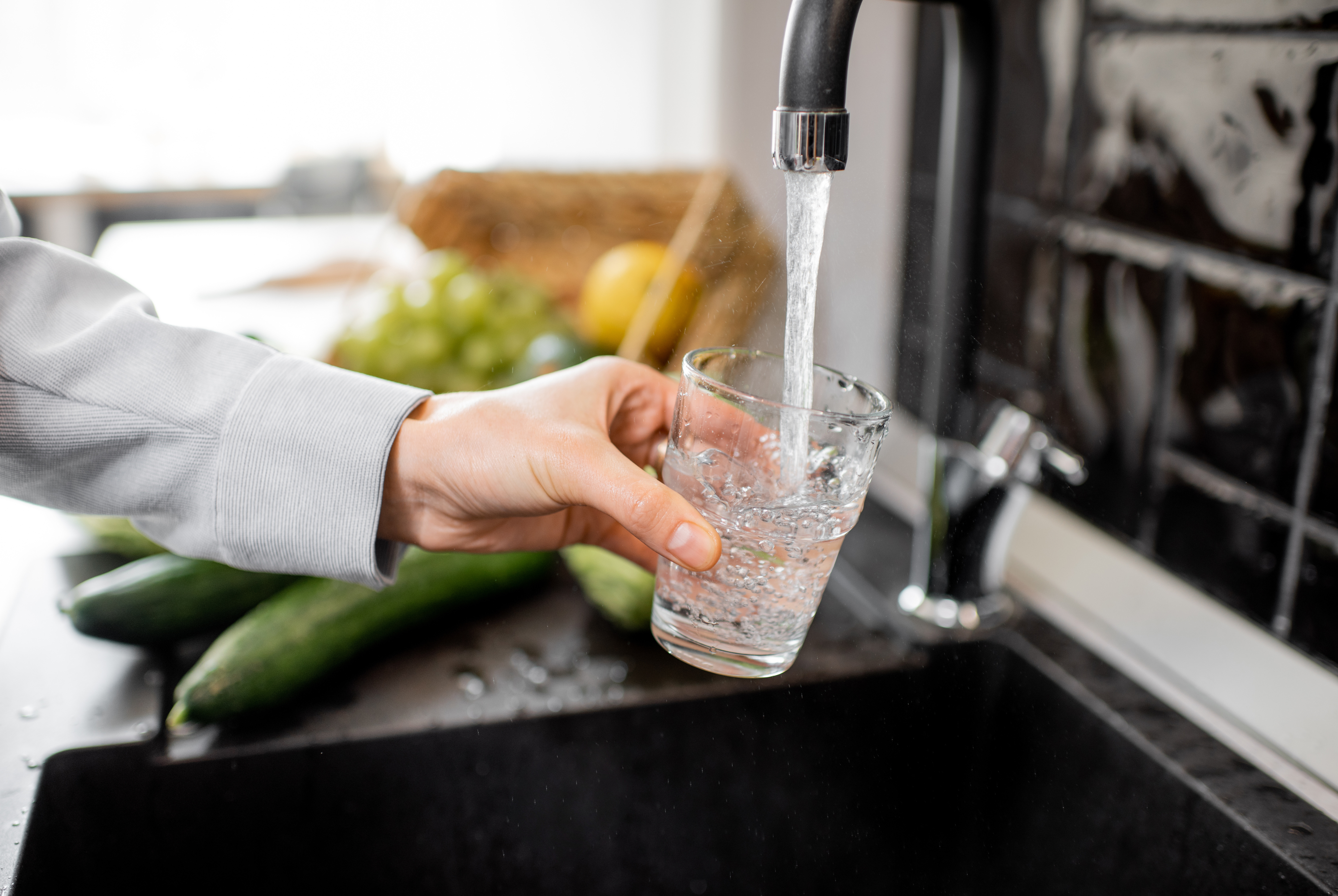 A person filling a clear cup with water from the kitchen's faucet.